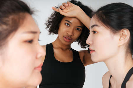 Diversity concept. Portrait of african women in black sport bra with face of asian people on side on white backgroundの写真素材