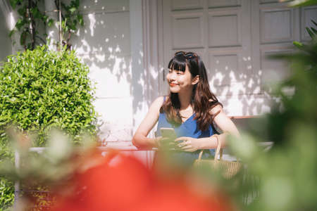 Cheerful happy young asian woman traveler wearing blue dress booking hotel or order stuff with online service with smartphone.の写真素材