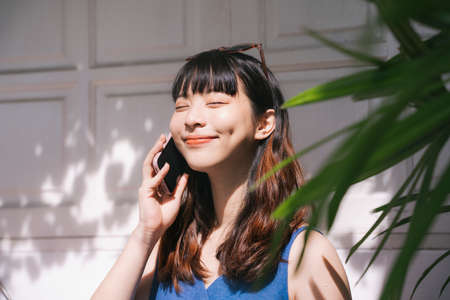 Cheerful young asian woman traveler wearing blue dress talking on the phone and smile.の写真素材