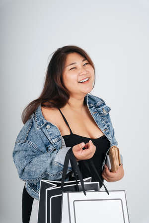 Portrait of fat woman in black dress and jeans jacket holding shopping paper bags isolate over white background.の写真素材