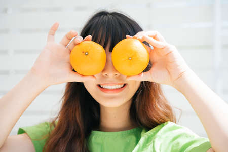 Young asian woman traveler wearing green shirt holding orange fruits at eyes.