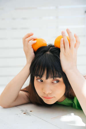 Young asian woman traveler wearing green shirt holding orange fruit over her head.の写真素材