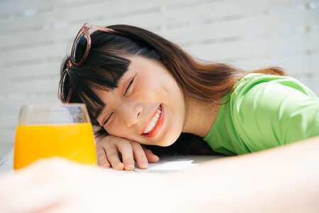 Cheerful young asian woman traveler wearing green shirt and sunglasses enjoy drinking healthy orange juice.の写真素材
