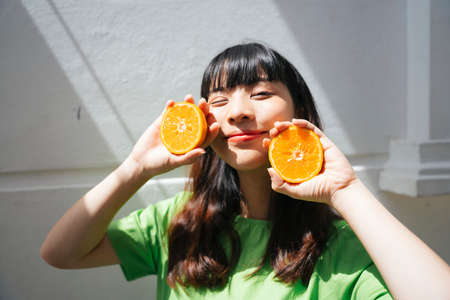 Portrait of young asian woman wearing green shirt holding slice of oranges.の写真素材