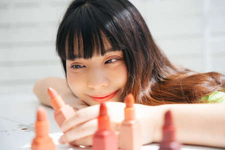 Close up portrait of young asian woman looking at lipsticks on table. Cosmetic for girl concept.の写真素材