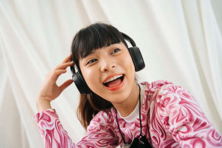 Close up portrait of young asian woman in pink shirt enjoy listen to music with headphone.の写真素材