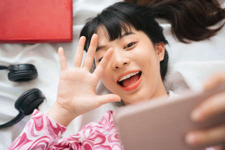Top view - Young asian woman in pink shirt taking selfie on a bed with smartphoneの写真素材