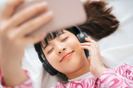 Top view - Young asian woman in pink shirt enjoy listen to music with headphone and smartphone....