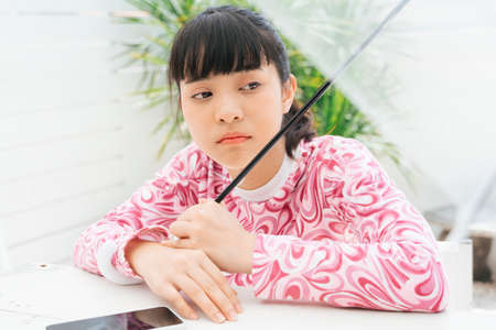 Unhappy young asian woman in pink shirt holding transparent umbrella with smartphone on table.の写真素材