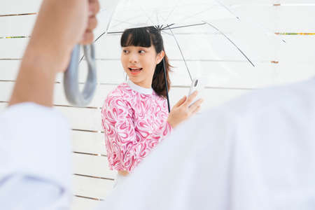 Young asian woman in pink shirt holding transparent umbrella and talking on the phone. Boyfriend waiting for her finish the phone call.の写真素材