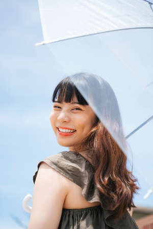 Young asian woman traveler holding transparent umbrella outdoors in sunny day.の写真素材