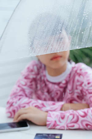 Moody asian woman in rainy day with smartphone and credit card on table.の写真素材