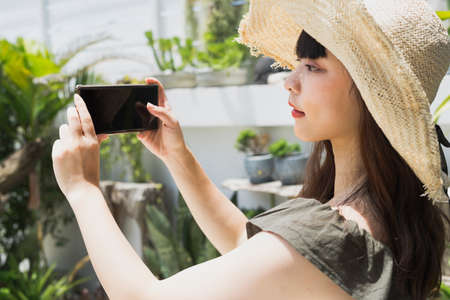 Young asian woman wearing hat holding smartphone at yard.の写真素材