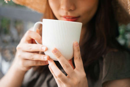 Close up - Young asian woman traveler wearing straw hat enjoy drinking coffee outdoors.