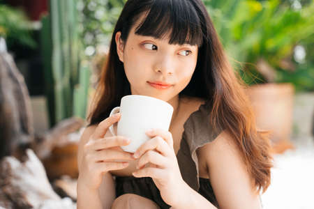 Cheerful young asian woman holding a cup of coffee at yard.の写真素材