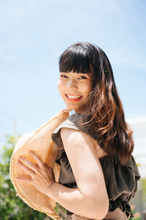 Side view - Cheerful young asian woman holding a hat outdoors. Summer traveler concept.