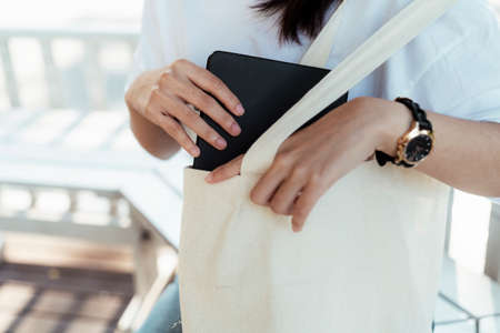 Cropped image of black notebook while a girl put it in white canvas bag.の写真素材