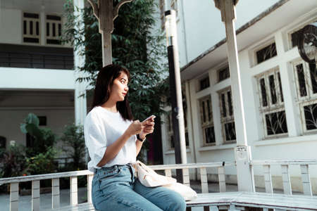 Cute girl in white t-shirt sitting in the pavilion at university park holding smartphone.