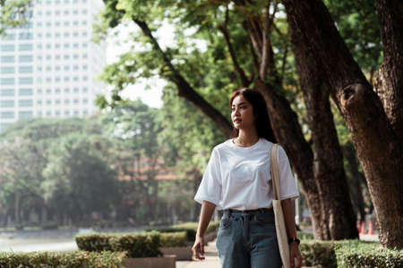 Cute girl in white t-shirt walking in the path with tree and bush in sunlight.の写真素材