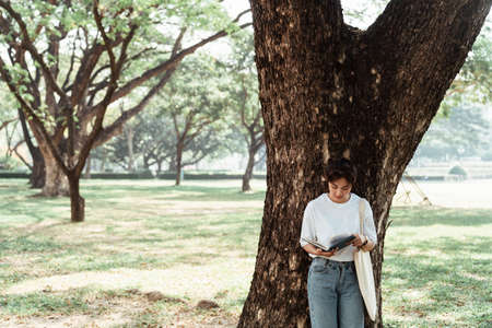 Cute girl in white t-shirt read the book at the big tree in the yard.