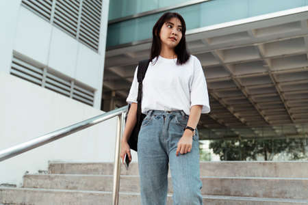 Cute girl in white t-shirt standing at the stair in front of the building.の写真素材