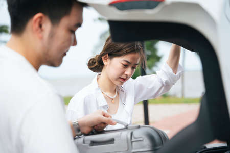 Beautiful asian woman putting luggage case inside car trunk with her boyfriend.
