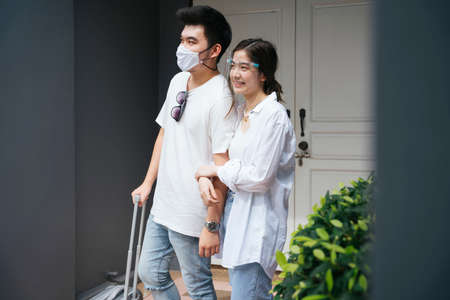 Lovely asian couple traveler wearing mask and faceshield at entrance door.