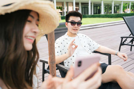 Handsome asian man wearing sunglasses sit on chair beach taking photo with girlfriend.の写真素材