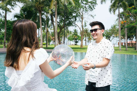 Asian couple traveler playing plastic ball in swimming pool.