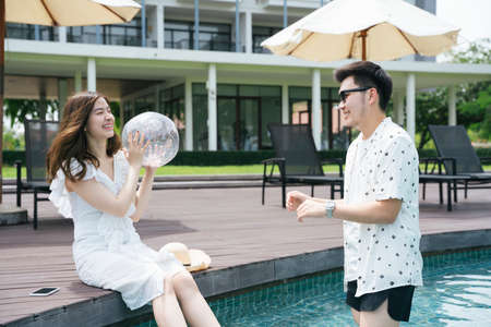 Romantic asian couple playing ball at hotel swimming pool.