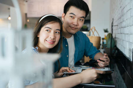 Asian couple traveler sitting on a bar ordering food on menu in restaurant.の写真素材