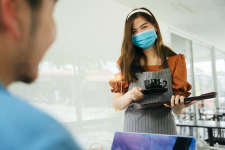 Asian waitress wear mask serving coffee cup to customer.の写真素材