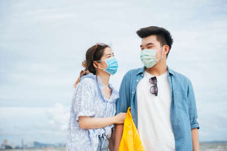 Asian couple traveler wearing mask walking on the beach.の写真素材