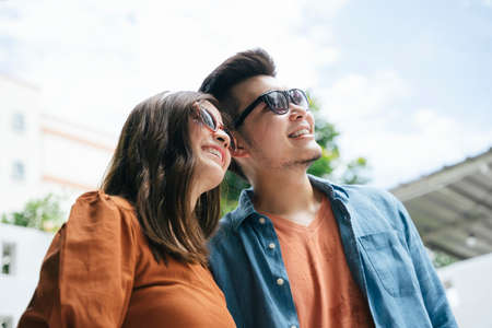Asian couple traveler wearing sunglasses walking in city. Both looking up the sky.