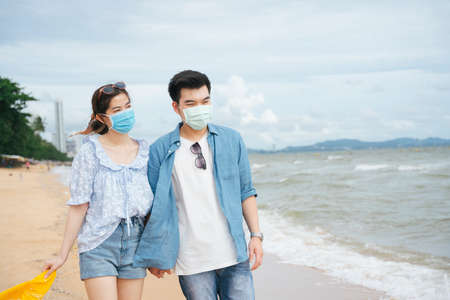 Asian couple traveler wearing mask walking on the beach.の写真素材