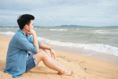 Lonely asian man sitting alone looking at the sea on the beach in summer.の写真素材