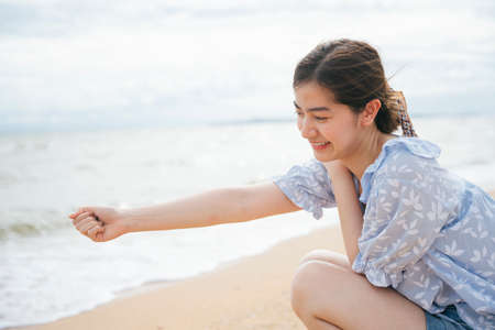 Beautiful asian woman grab a pile of sand on the beach.の写真素材