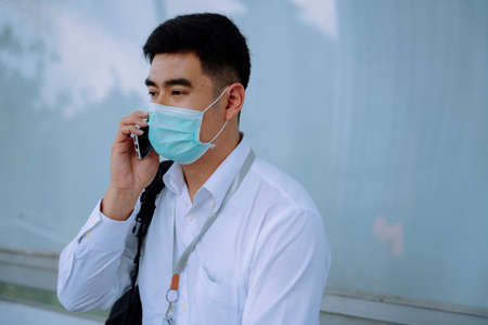 Business man wear mask using smartphone waiting for transportation at bus stop.の写真素材