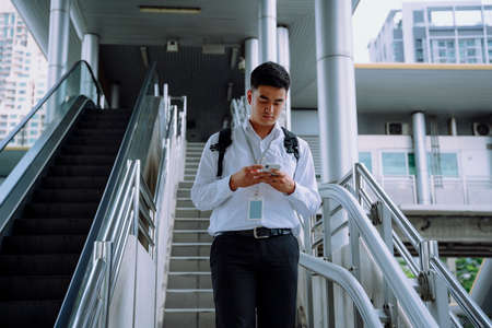 Asian business man using smartphone and walking down stair in city.