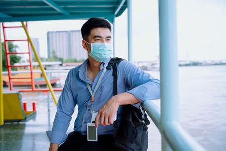 Asian business man wear mask waiting for a boat public transportation in Bangkok.