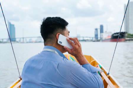 Back view - Asian business man talking on the phone travel by a boat in Bangkok, Thailand.