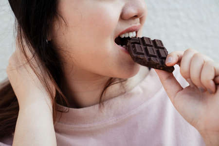 Cropped image of dark chocolate bar is eaten by the fat woman in pink t-shirt.の写真素材