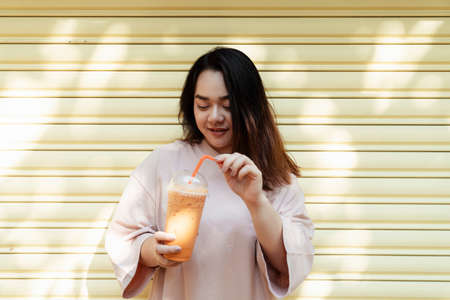 Happy fat woman enjoy Thai milk tea in a plastic cup with orange straw.の写真素材
