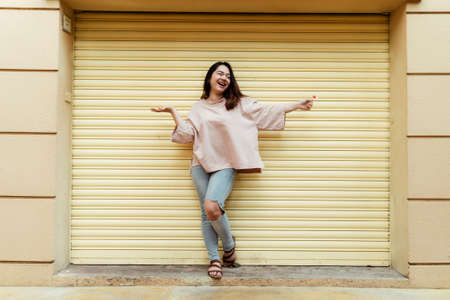 Happy long hair fat woman standing at the yellow shuter door between beige wall.の写真素材