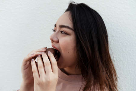 Happy fat woman enjoy eating choco pie in front of white wall.の写真素材