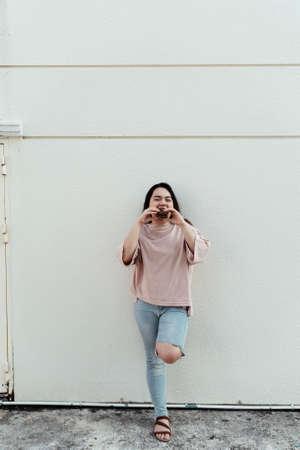 Long hair fat woman eat two choco pie in the same time while standing in front of white wall.の写真素材