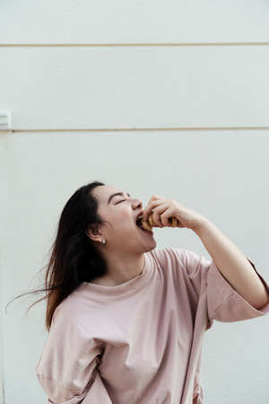 Long hair fat woman enjoy eating biscuit with jam while she standing in front of white wall.の写真素材