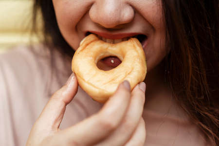 Cropped image of plain donut is bitten by the fat woman's mouth.