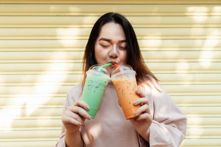 Happy fat woman drink iced Thai tea and iced green tea with straw in the same time.の写真素材