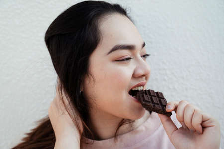 Long hair fat woman touch her hair while eating dark chocolate bar.の写真素材